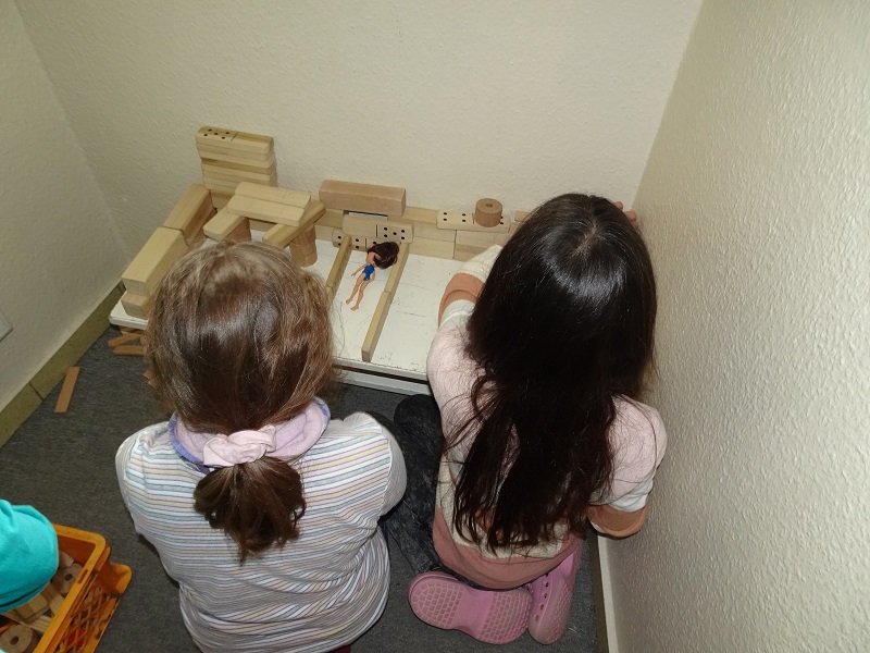 Zwei Mädchen bauen für ihre Puppen ein Bett aus Bausteinen